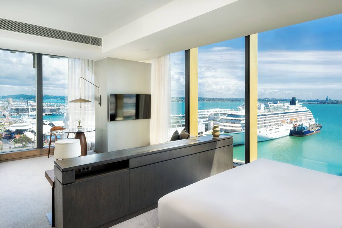Ein modernes Hotelzimmer mit einem großen Fenster und Blick auf ein Kreuzfahrtschiff und die Skyline der Stadt.