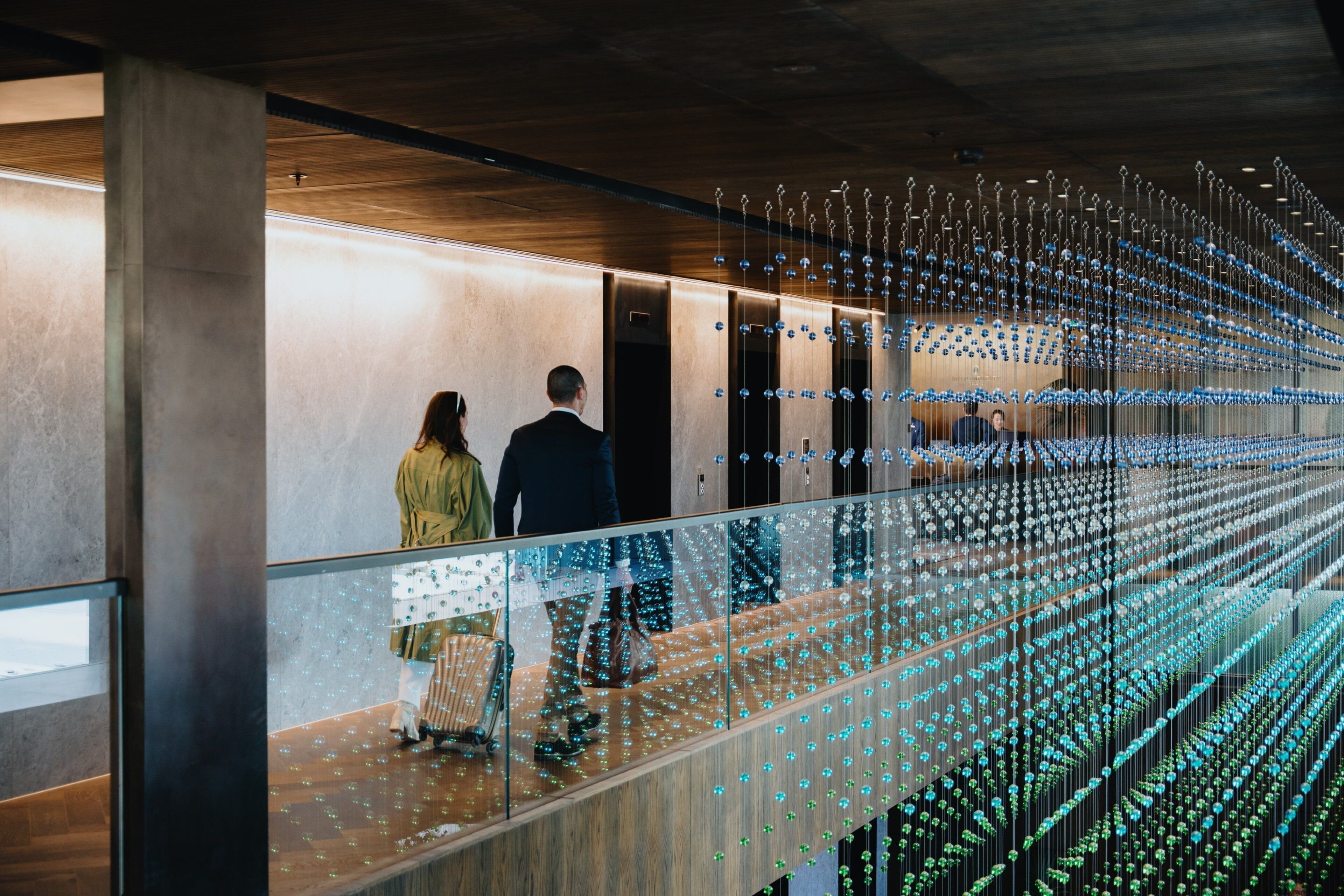 A modern hotel lobby with a glass partition and a ceiling adorned with hanging lights.