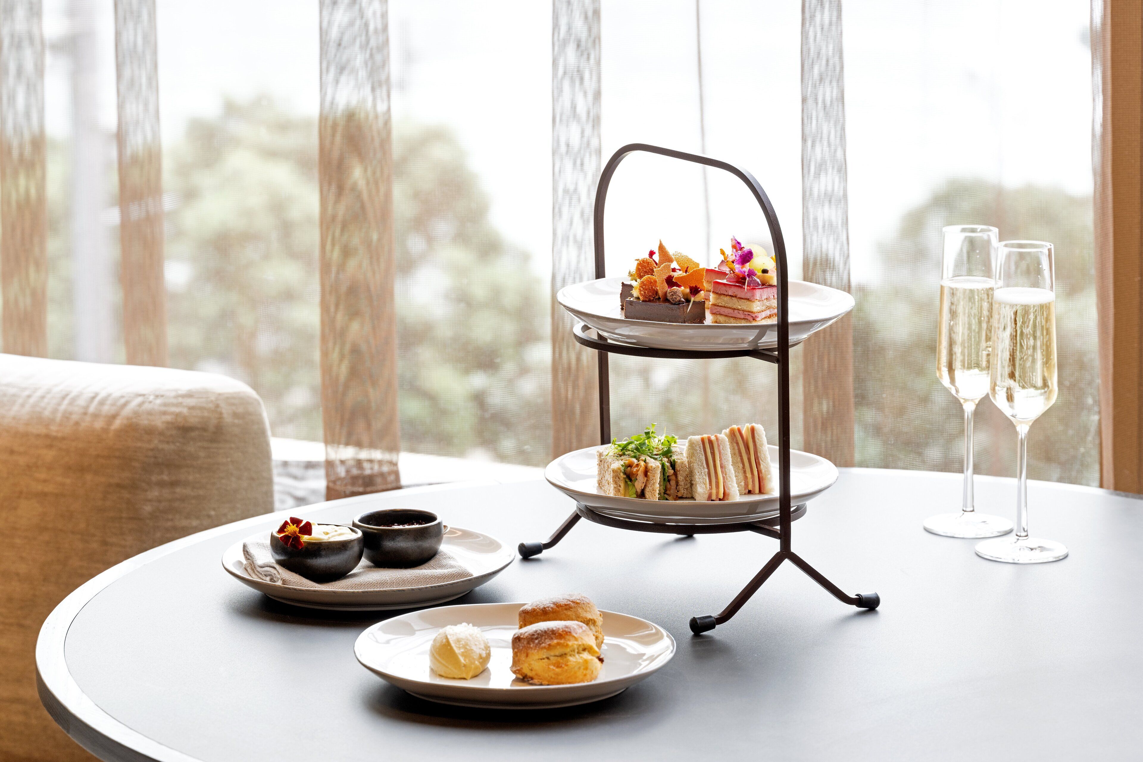 A three-tiered dessert stand with sandwiches and scones on a table by a window.