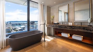 Un baño moderno con una bañera independiente, un espejo grande y vistas a un puerto deportivo y edificios.