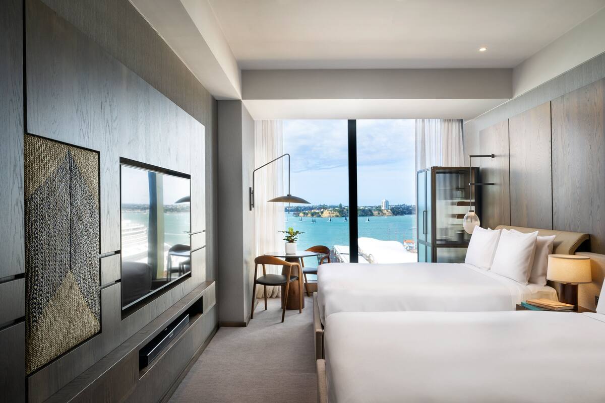 Ein modernes Hotelzimmer mit zwei Betten, einem Fernseher und Blick aufs Meer.
