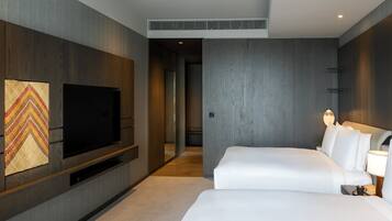 A modern hotel room with a large flat-screen TV mounted on the wall, a bed with white linens, and a bedside table with a lamp.