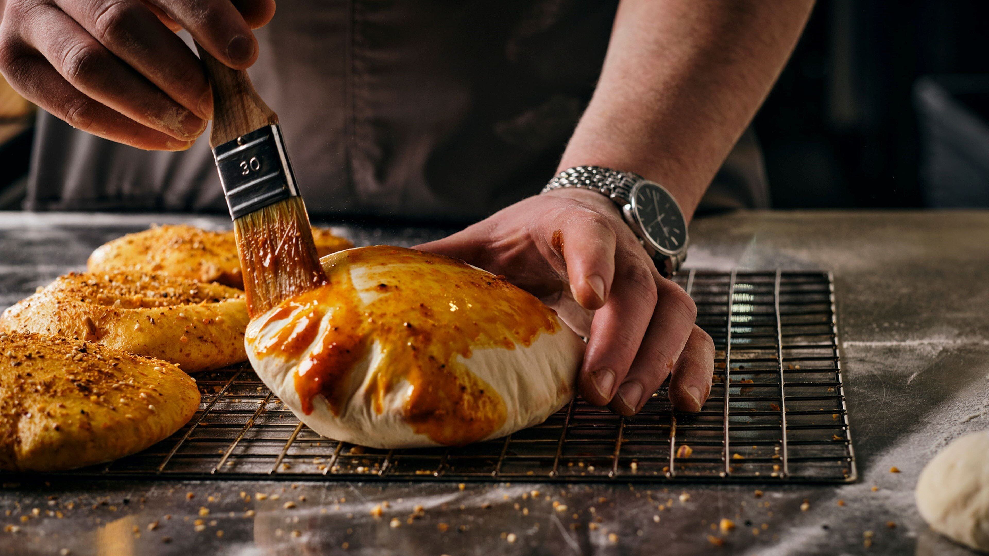 A person applying sauce to a bread on a cooling rack.