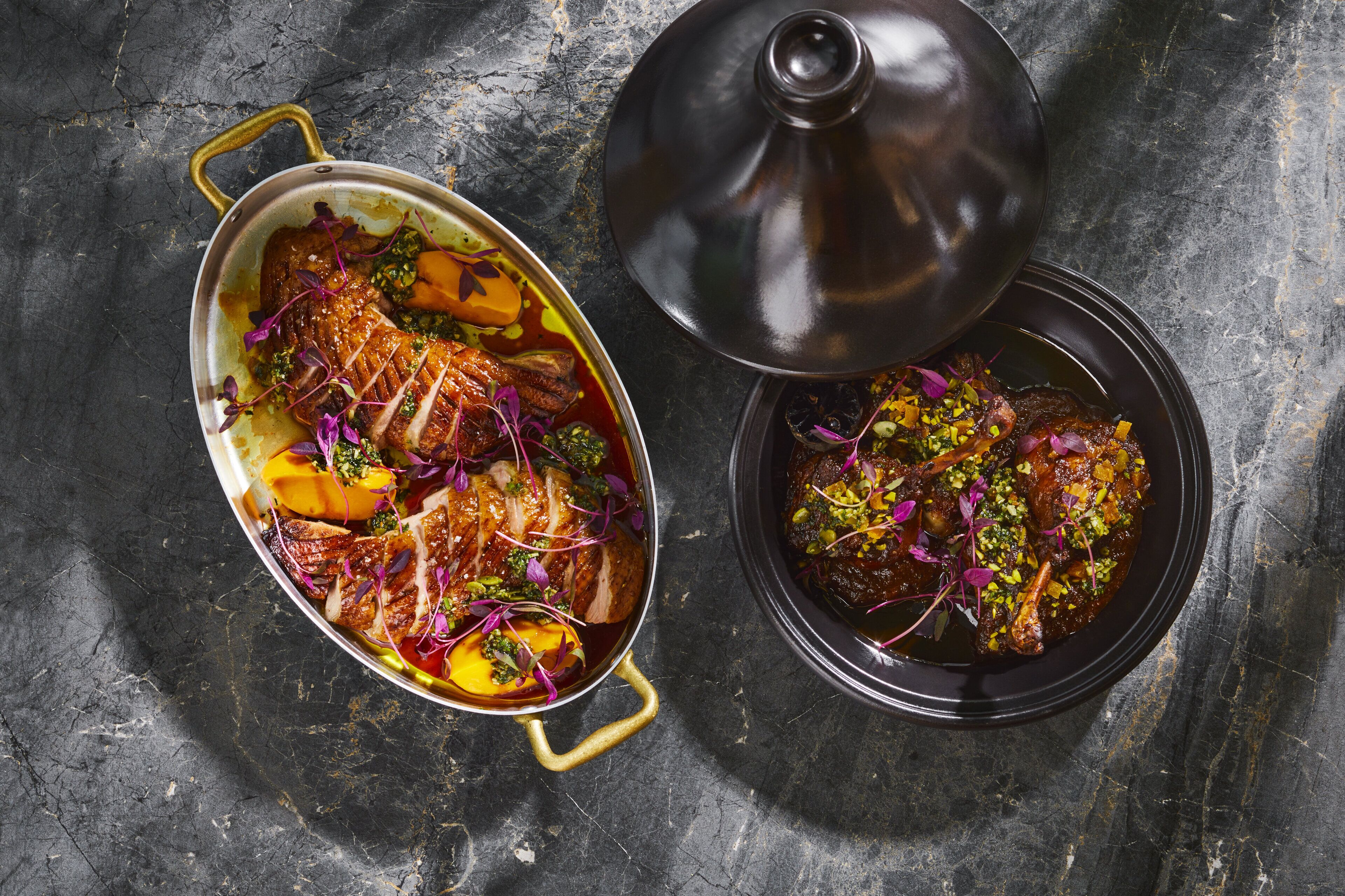 Un plat composé de viande et de légumes, agrémenté de fleurs violettes, et servi sur une assiette ou un plat de couleur sombre.