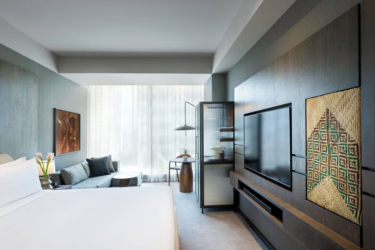 Ein modernes Hotelzimmer mit einem großen Bett, einem Fernseher, einer Sitzecke und Blick auf die Stadt.