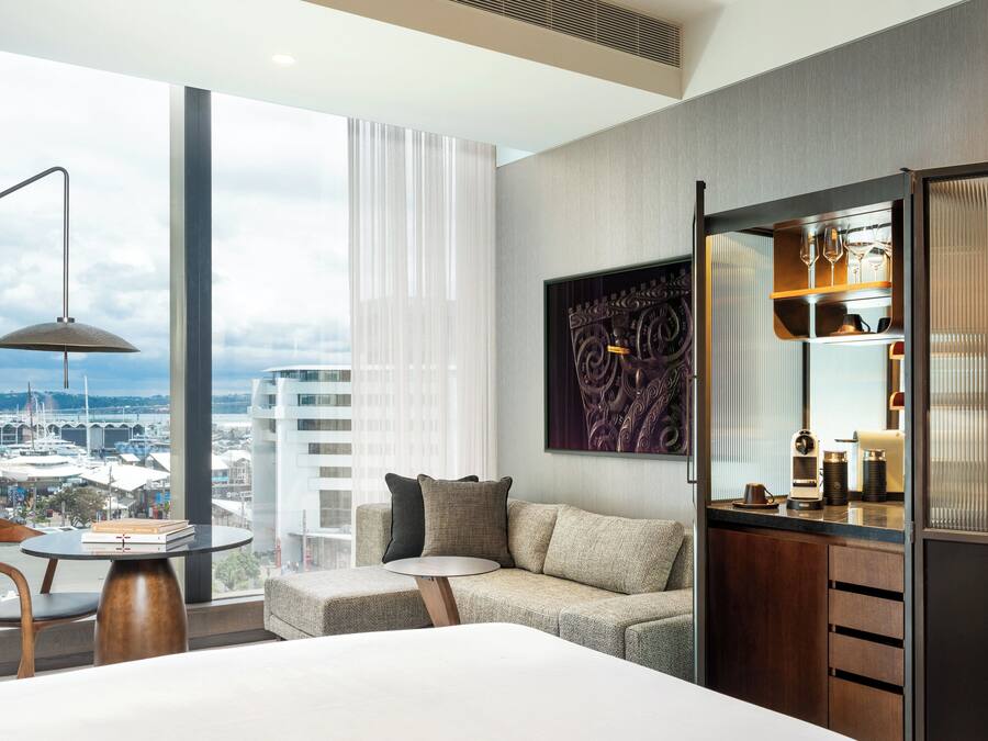 Una habitación de hotel moderna con un ventanal grande, un sofá, una mesita y un minibar.
