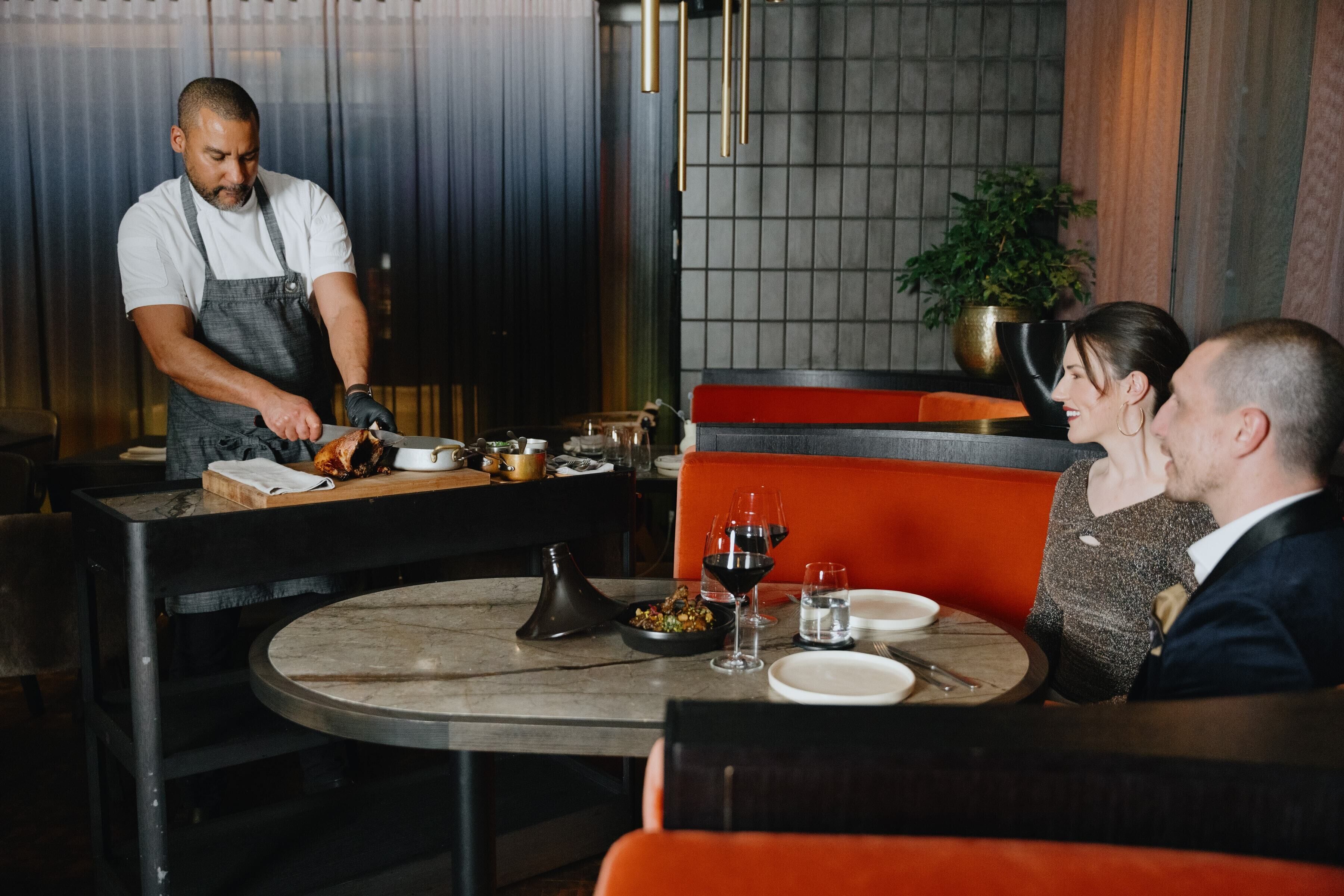 A restaurant interior with a waiter serving food to a couple seated at a table.