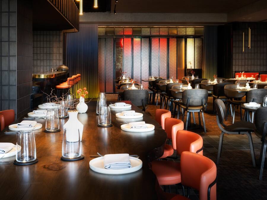 Un restaurant avec une longue table à manger dressée pour le repas, entourée de chaises.