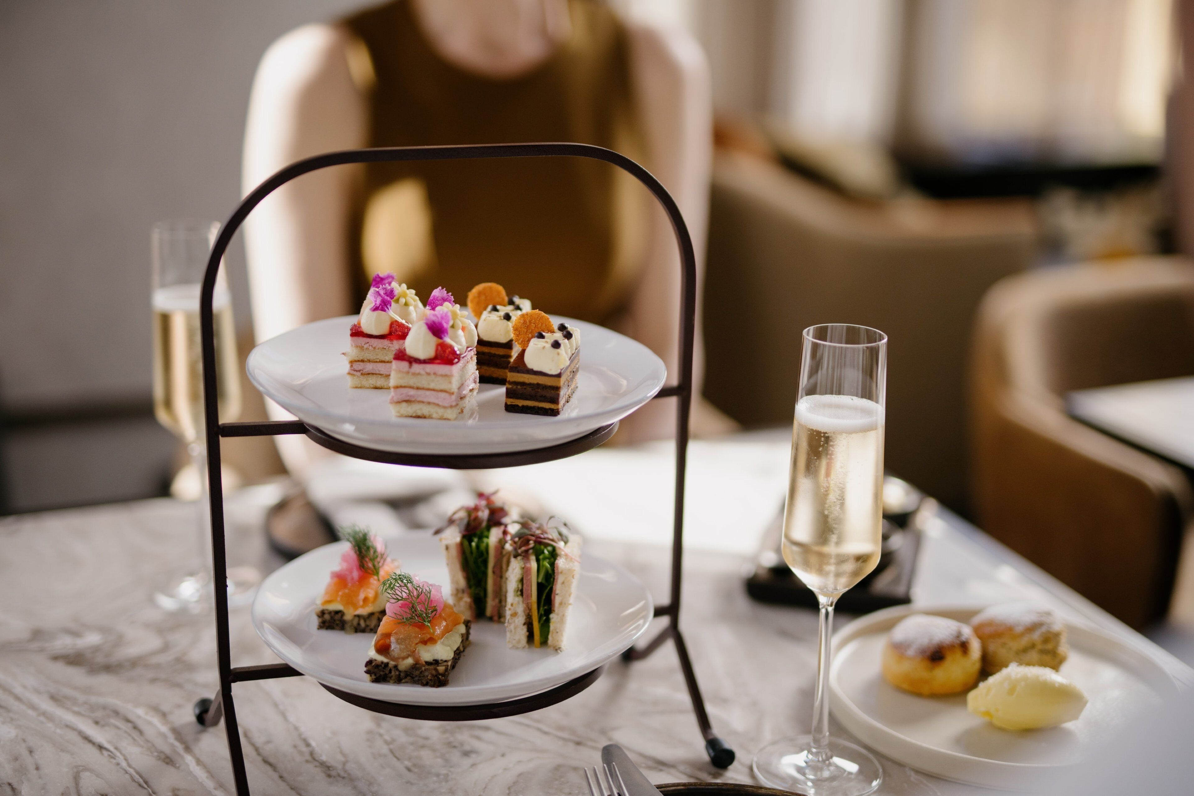 A three-tiered dessert stand with various pastries and a glass of champagne on a marble table.