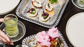 A dining table with a silver tray holding various appetizers and a glass of green beverage.
