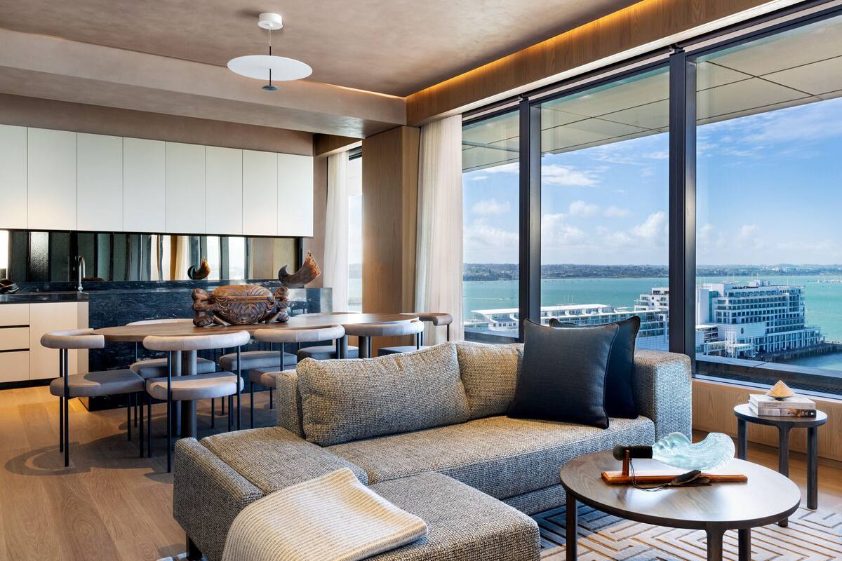 Ein modernes Wohnzimmer mit Sofa, Couchtisch und Essbereich. Ein großes Fenster bietet Blick auf die Stadt und das Wasser.