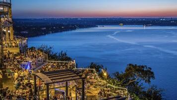 A waterfront restaurant with outdoor seating overlooking a large body of water, surrounded by city lights.