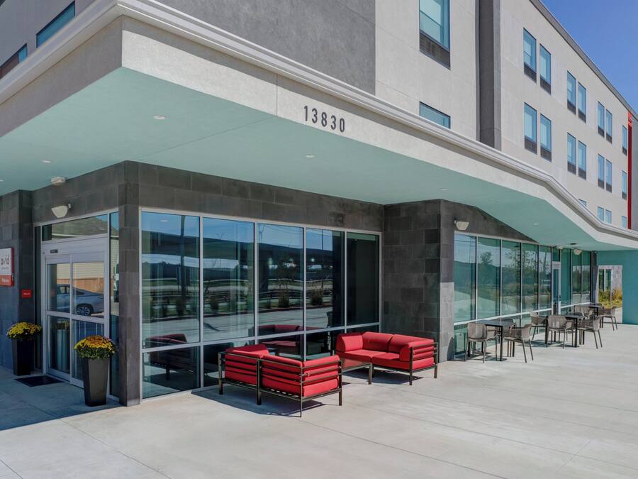 A modern building with a glass facade, numbered 13830, featuring outdoor seating and a clear view of the interior.