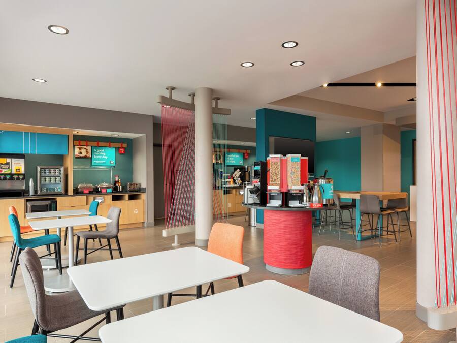 A modern restaurant with white tables and chairs, a kitchen area, and a colorful decor.