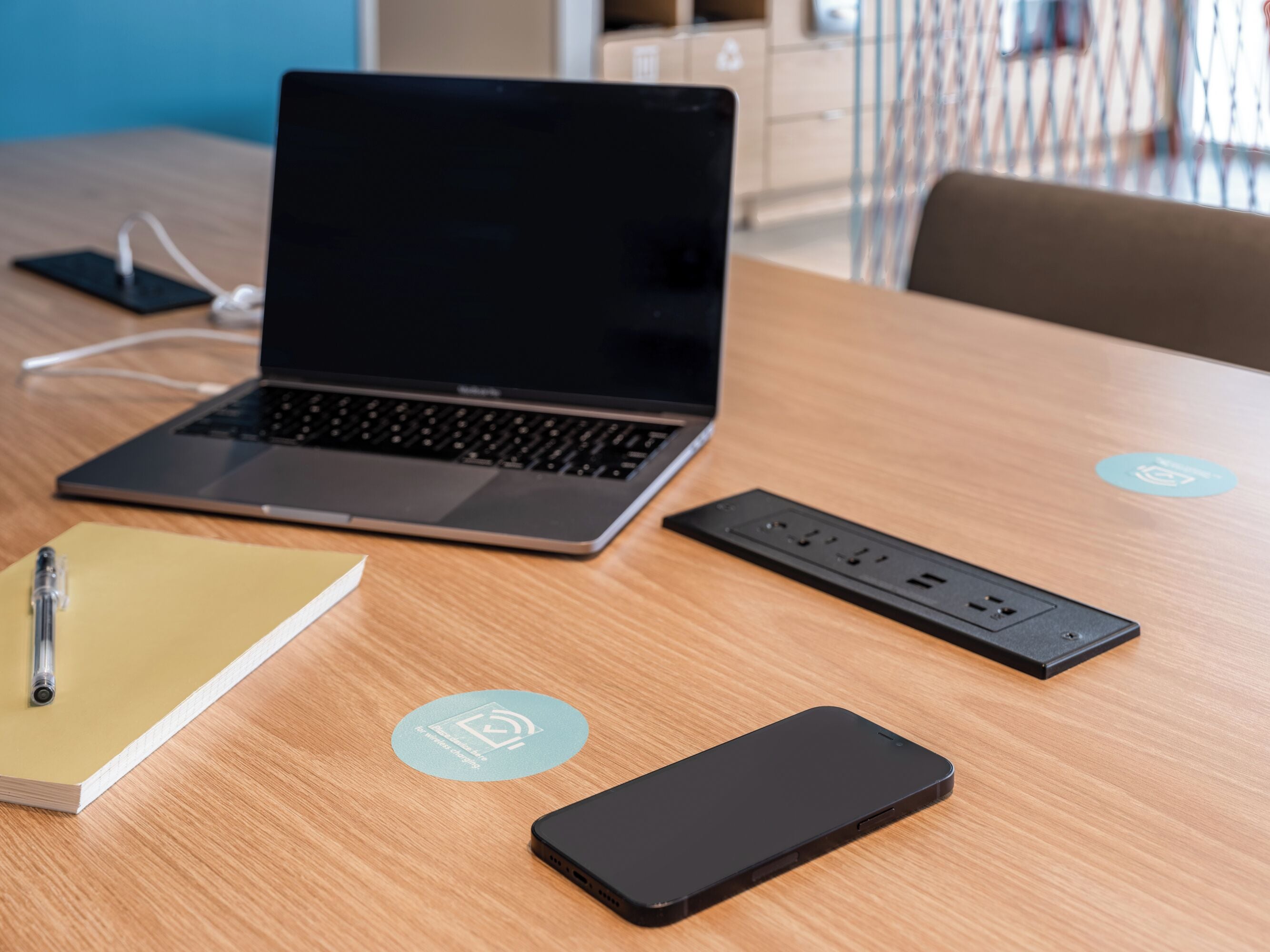 Una computadora portátil sobre una mesa de madera con un cuaderno, un teléfono inteligente y una regleta eléctrica.