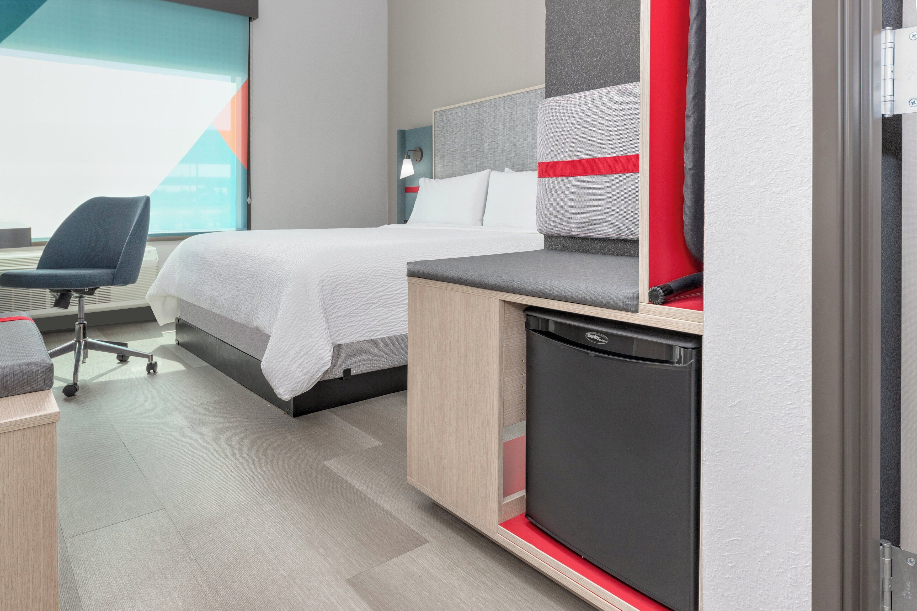 Una habitación de hotel moderna con cama, escritorio, silla y una kitchenette compacta.