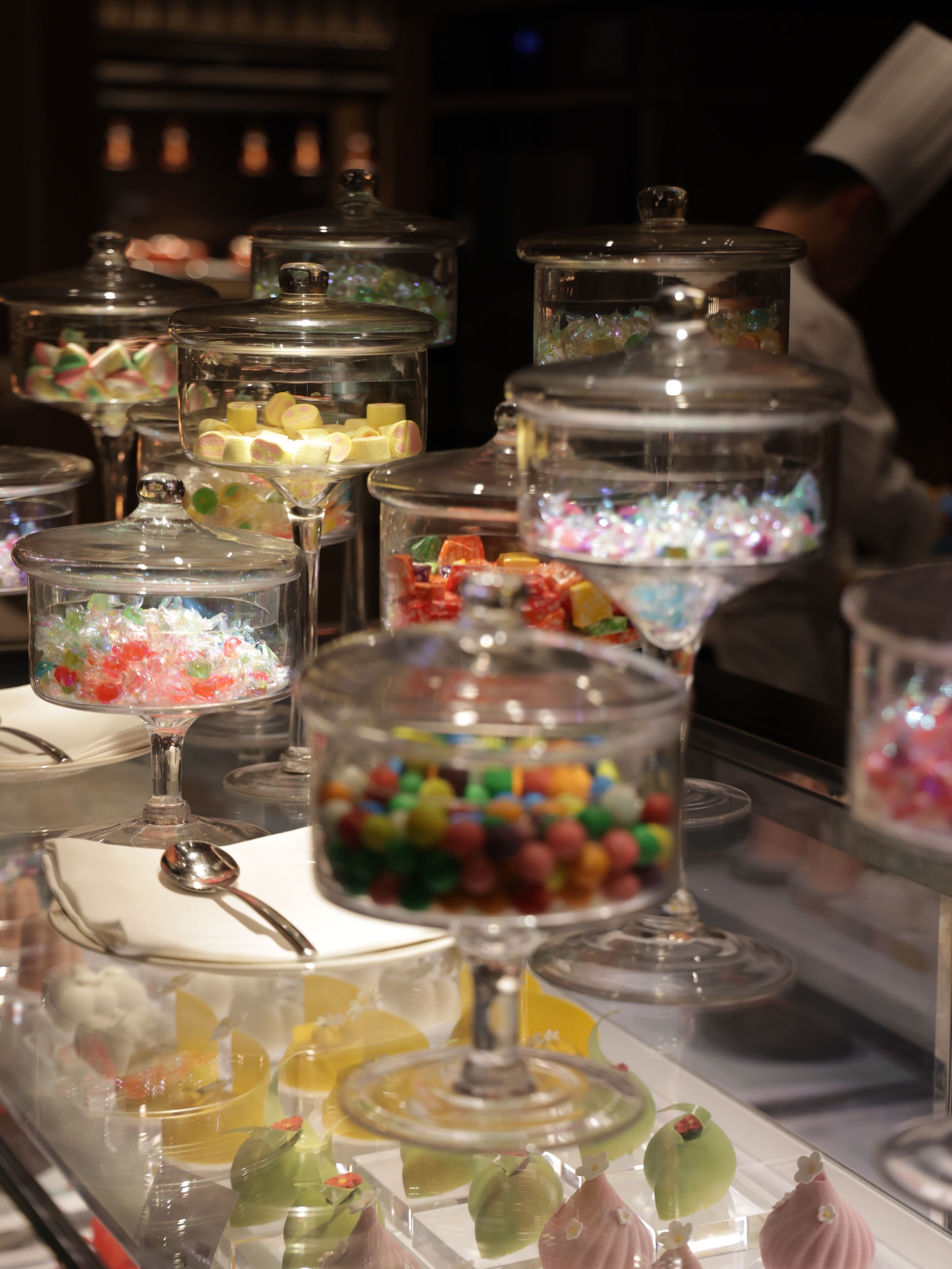 A buffet with various food items in glass containers and a spoon on the table.