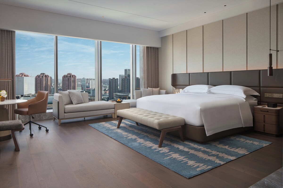 Habitación de hotel moderna con una cama grande, un sofá, un escritorio y vistas a la silueta urbana.