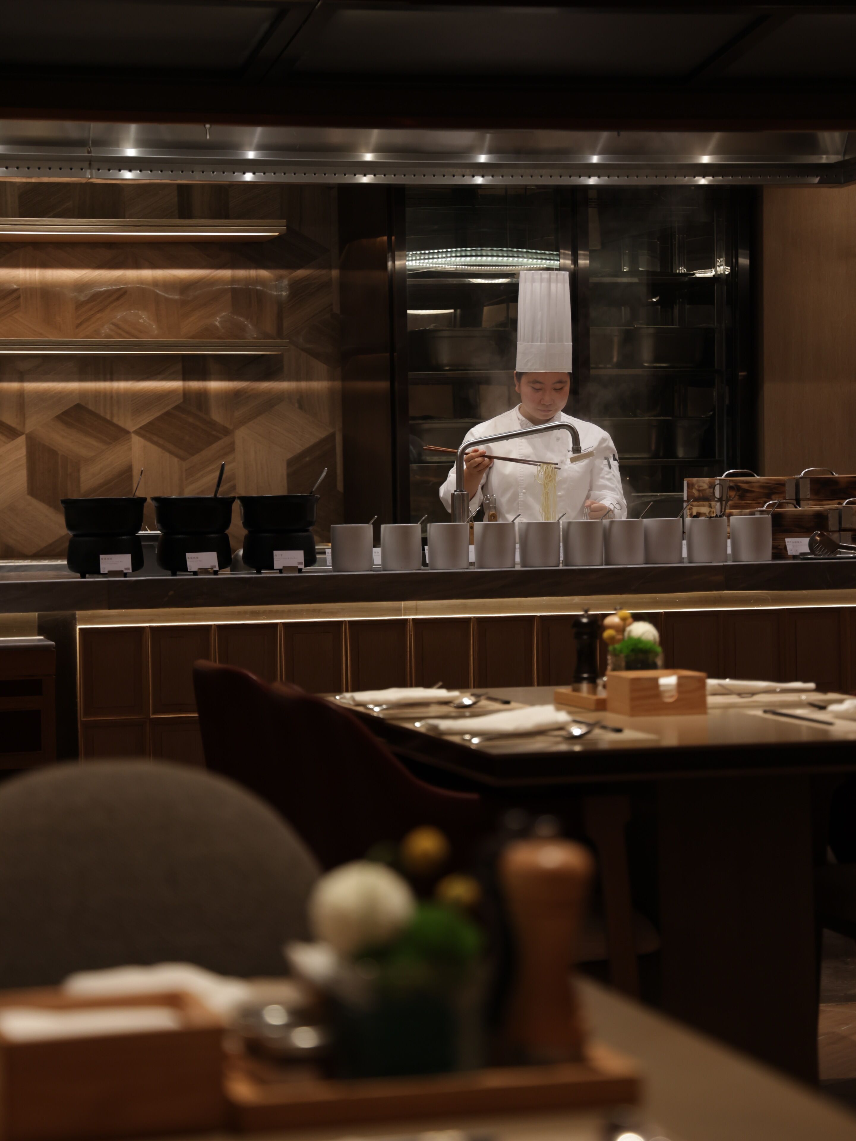A chef preparing food in a modern kitchen with wooden accents and stainless steel appliances.