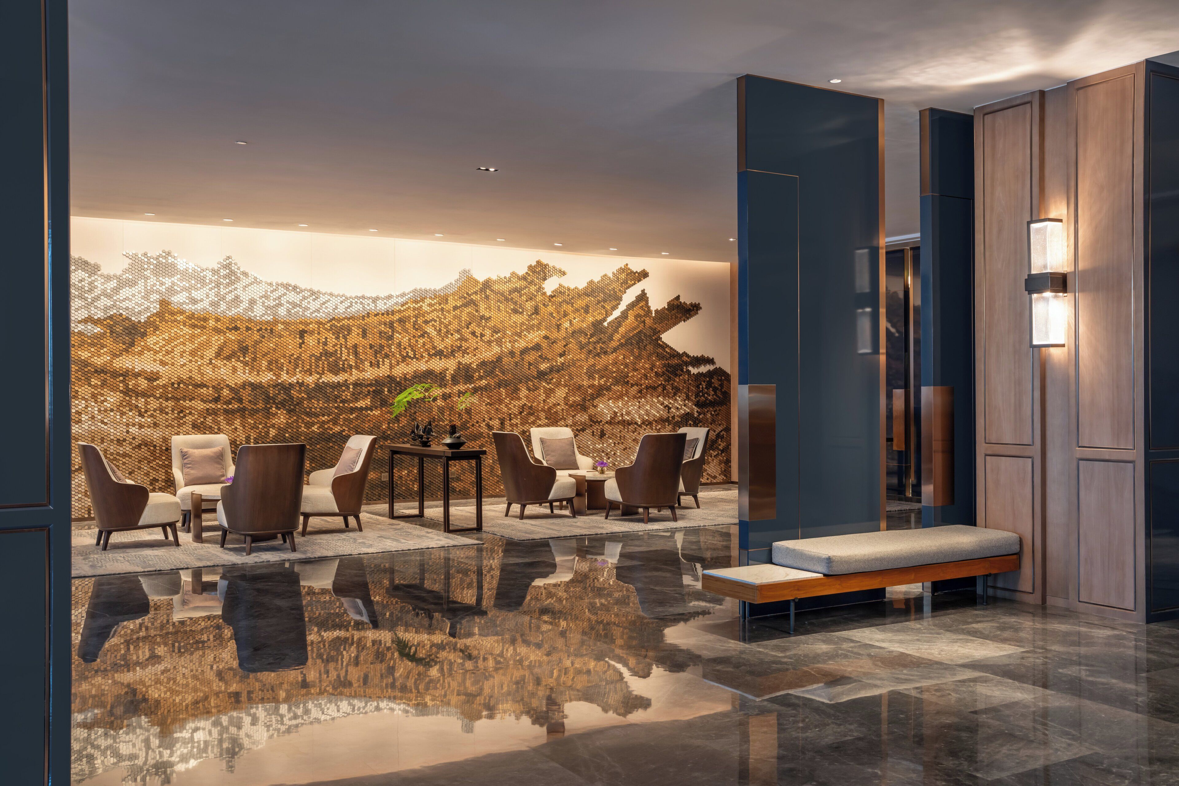 Een moderne lobby met een spiegelende vloer, een zithoek met stoelen en een bank, een wand met een reliëfpatroon, en een trap.