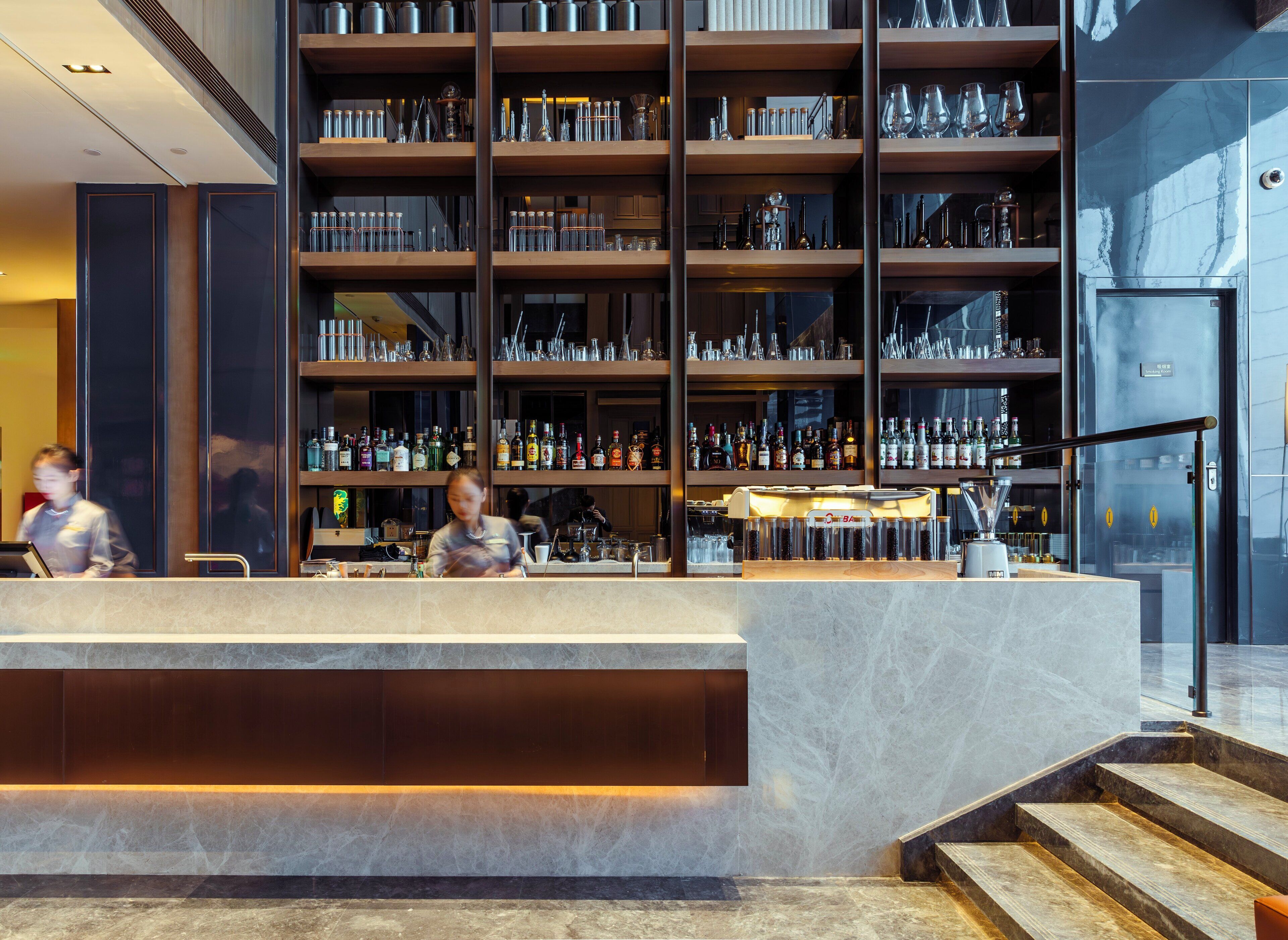 A bar area with shelves of bottles and glasses, a bar counter, and a staircase leading to an upper level.
