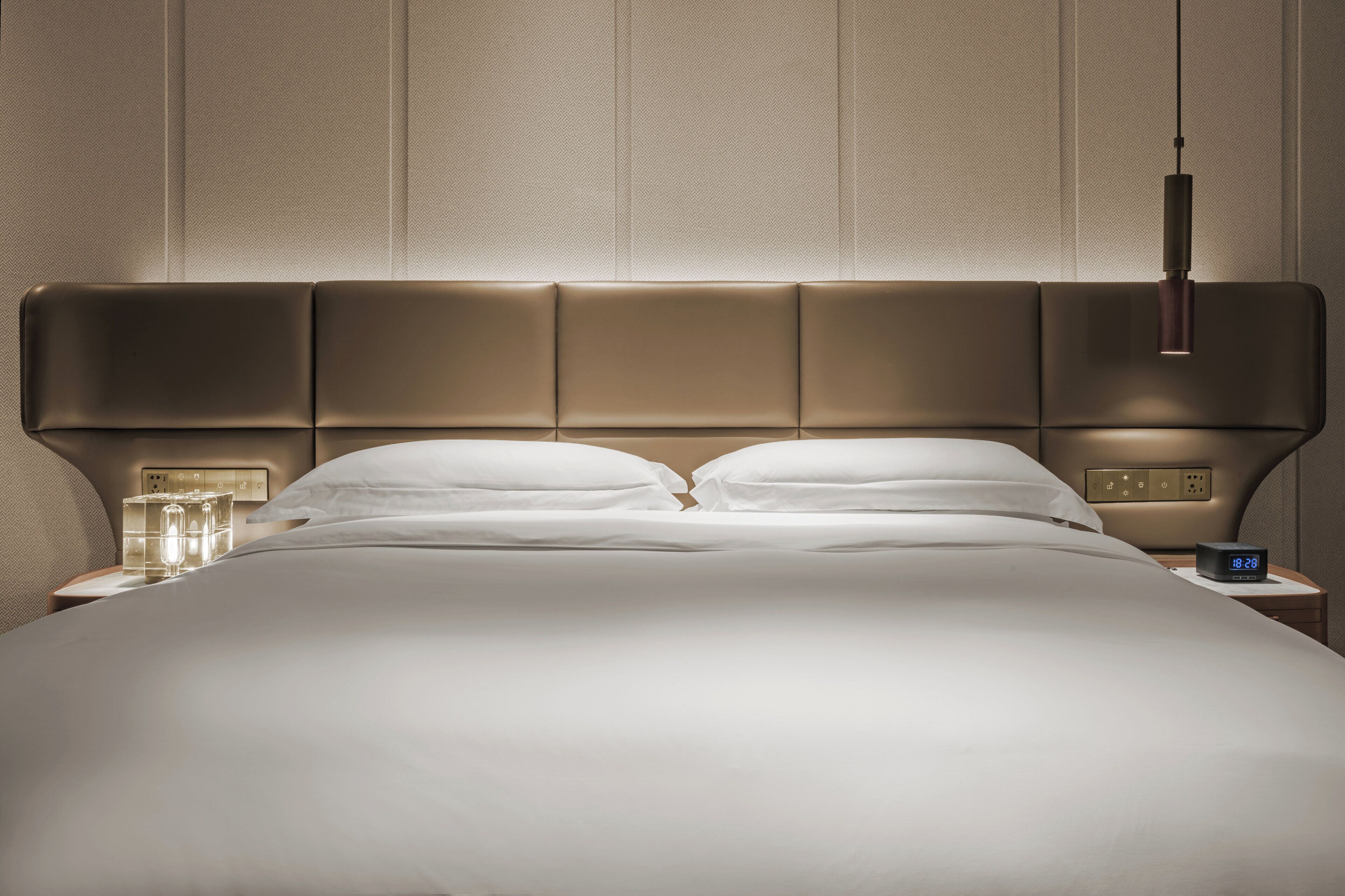 Une chambre d’hôtel moderne avec un grand lit, une table de chevet avec une lampe et une horloge numérique.