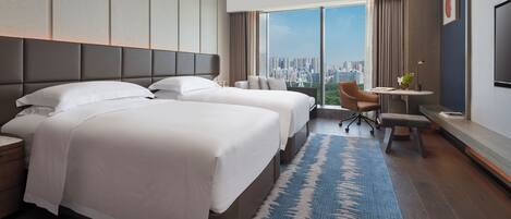 A hotel room with two beds, a desk, a chair, and a large window with a city view.