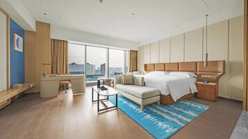 A modern hotel room with a large bed, a desk, a sofa, and a view of the city.