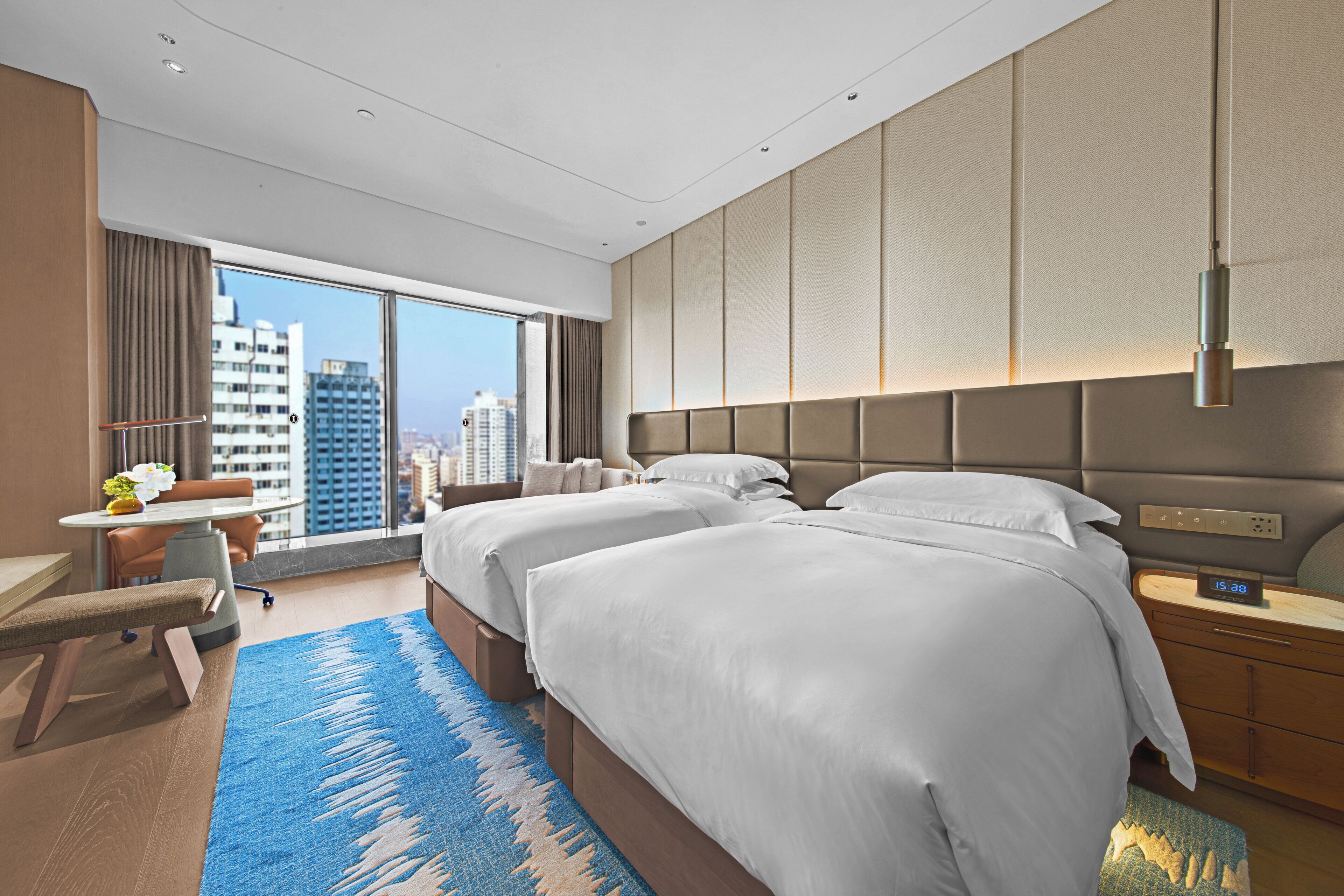 Ein modernes Hotelzimmer mit zwei Betten, einem Schreibtisch und einem großen Fenster mit Blick auf die Stadt.