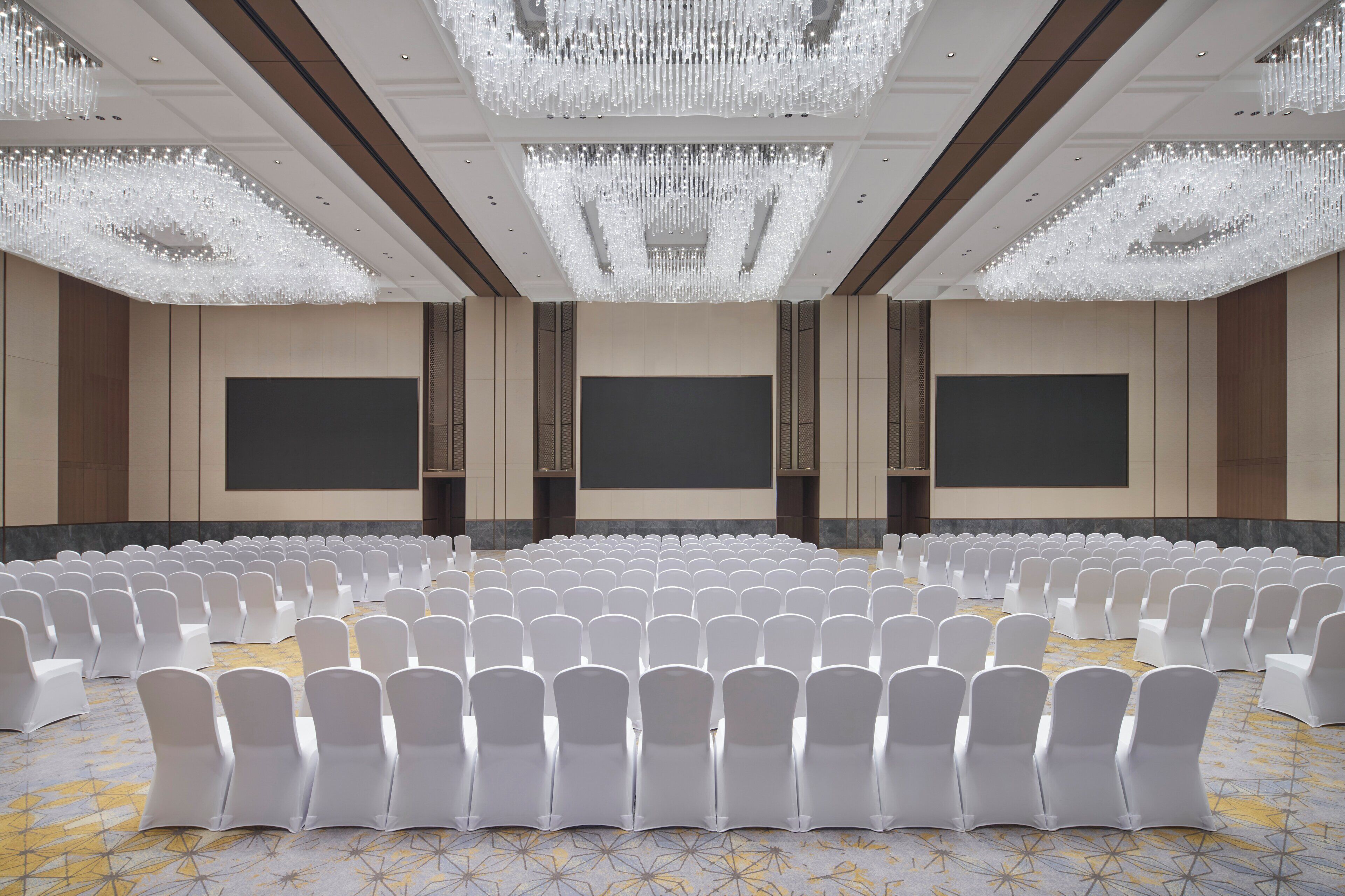 A large conference room with rows of white chairs, a large screen, and a chandelier.
