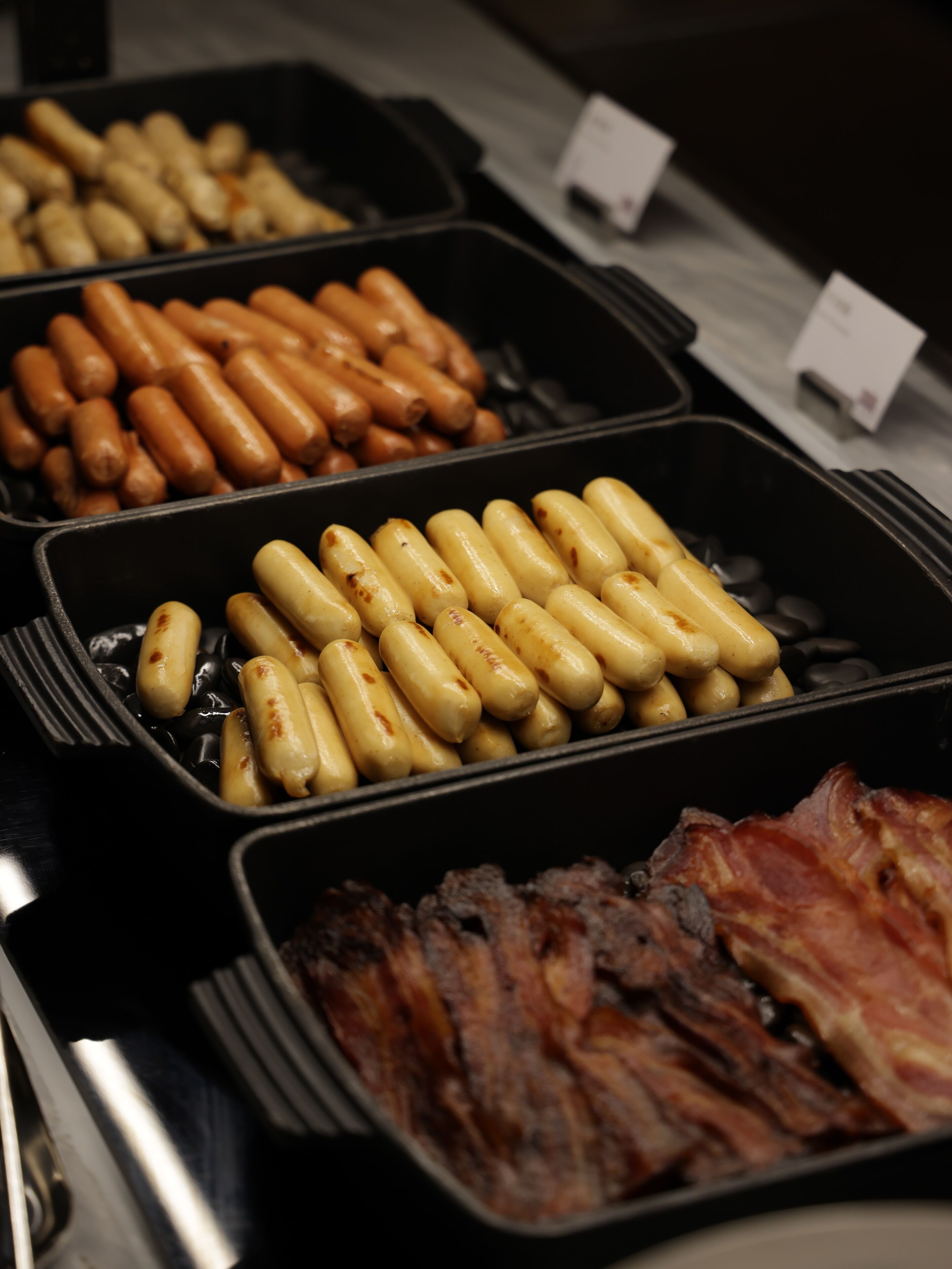 A buffet with various food items including sausages, potatoes, and bacon.