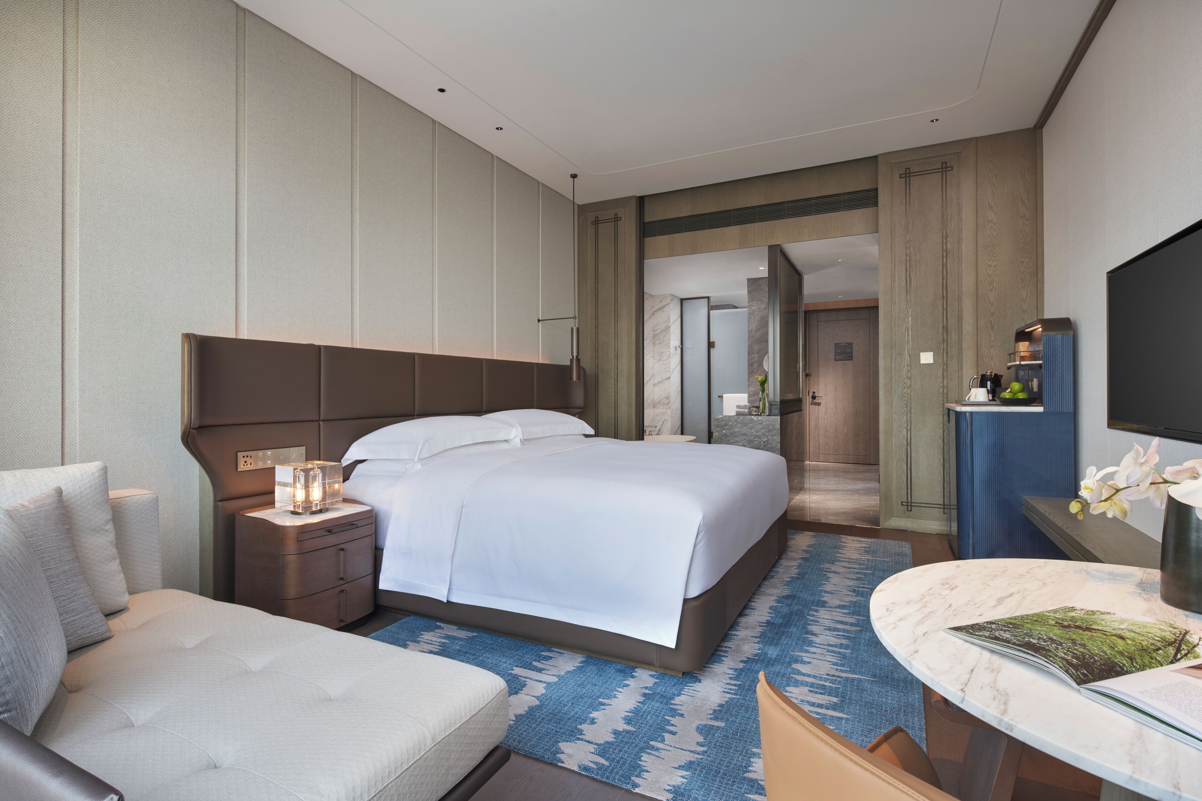 Ein modernes Hotelzimmer mit einem großen Bett, einer Sitzecke, einem Badezimmer und einem Fernseher.