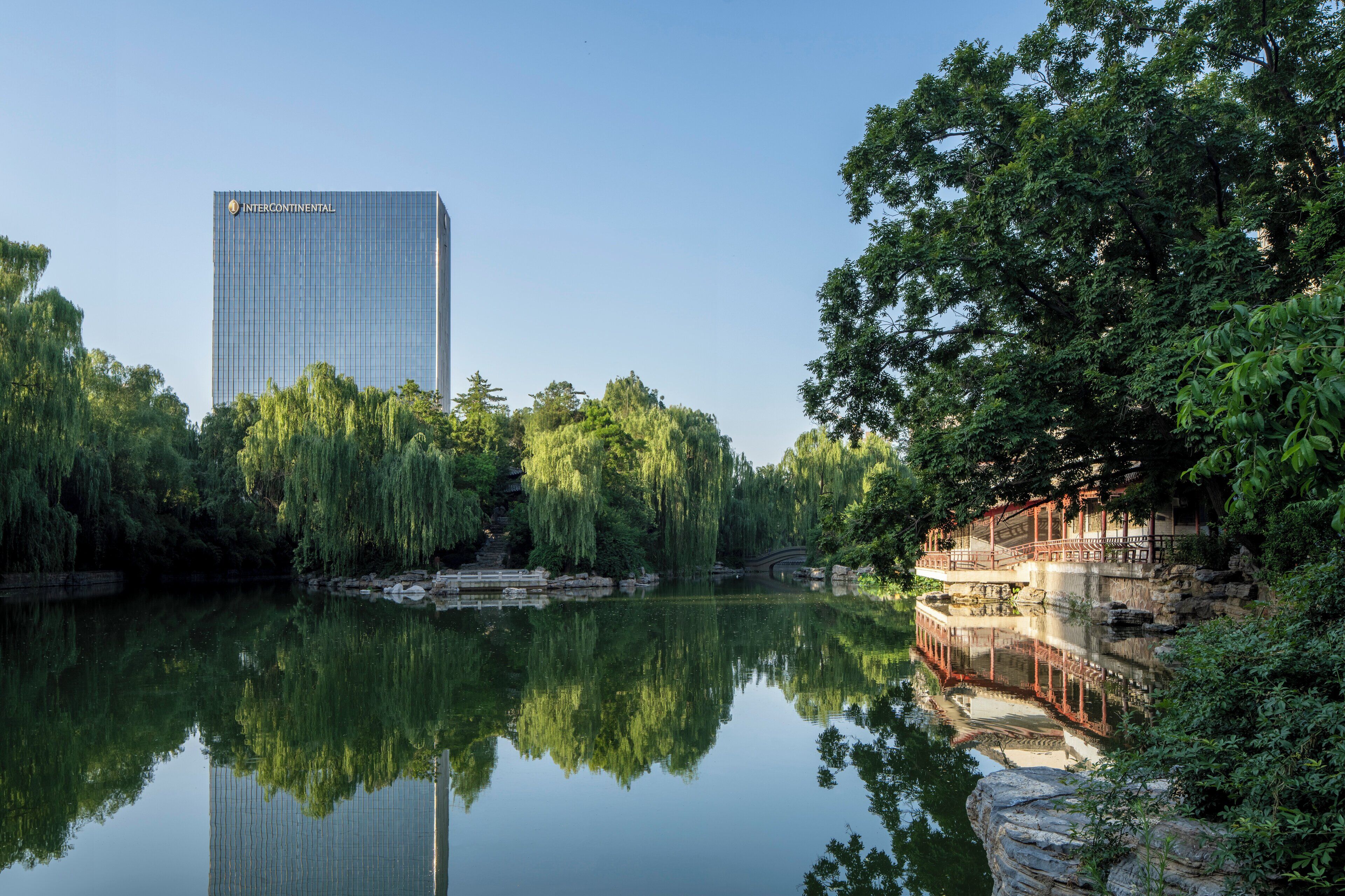 Un plan d’eau paisible, avec des reflets, une végétation luxuriante et un bâtiment moderne en arrière-plan.