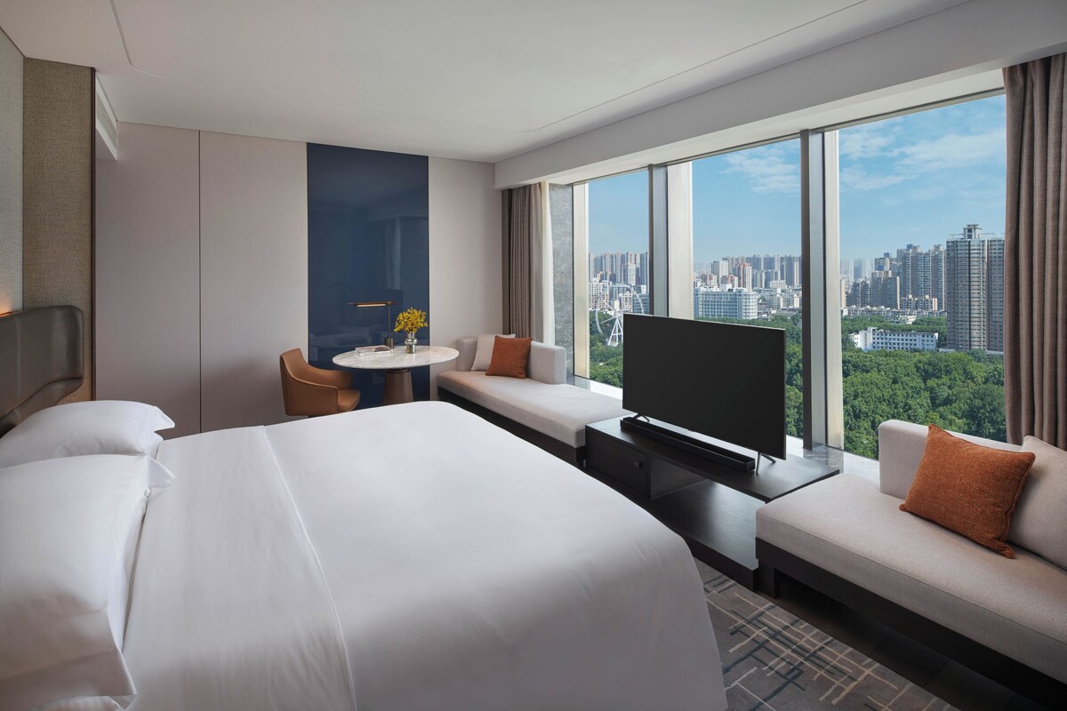 Habitación de hotel con una cama grande, un sofá, un televisor y vista a la ciudad.