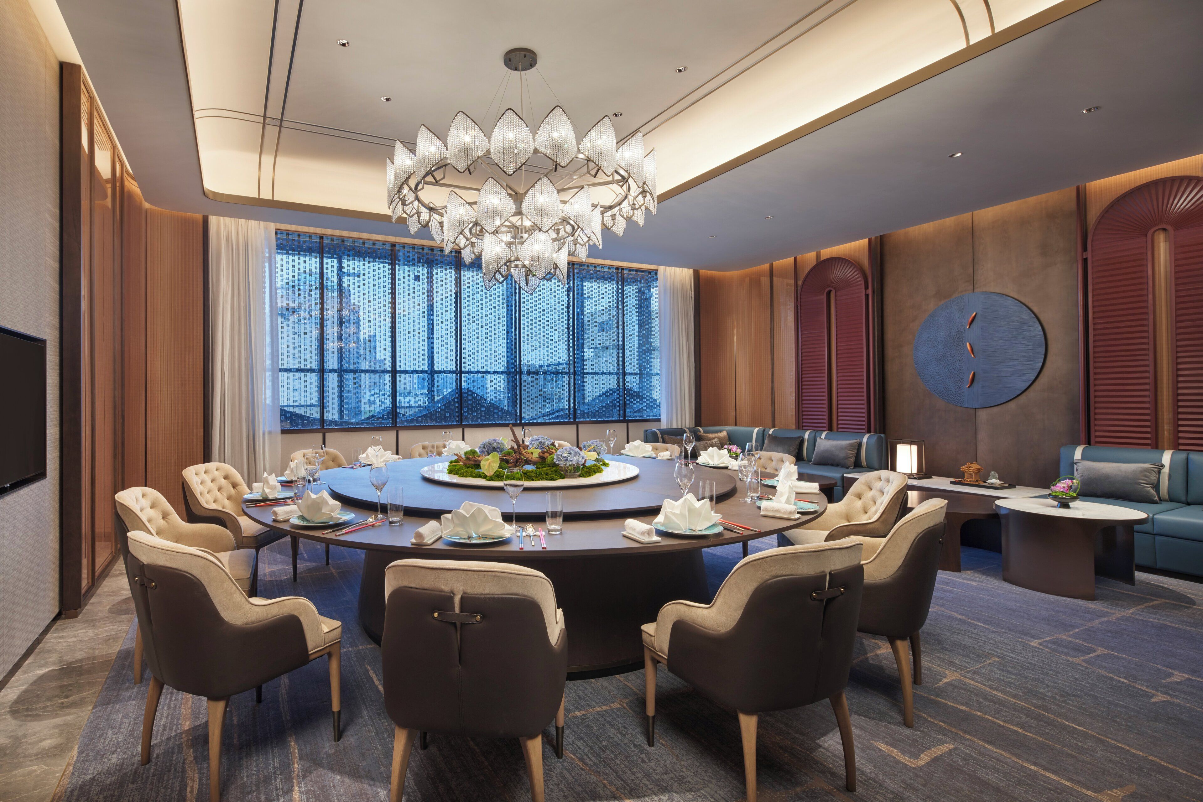 A modern conference room with a round table, comfortable seating, and a large chandelier.