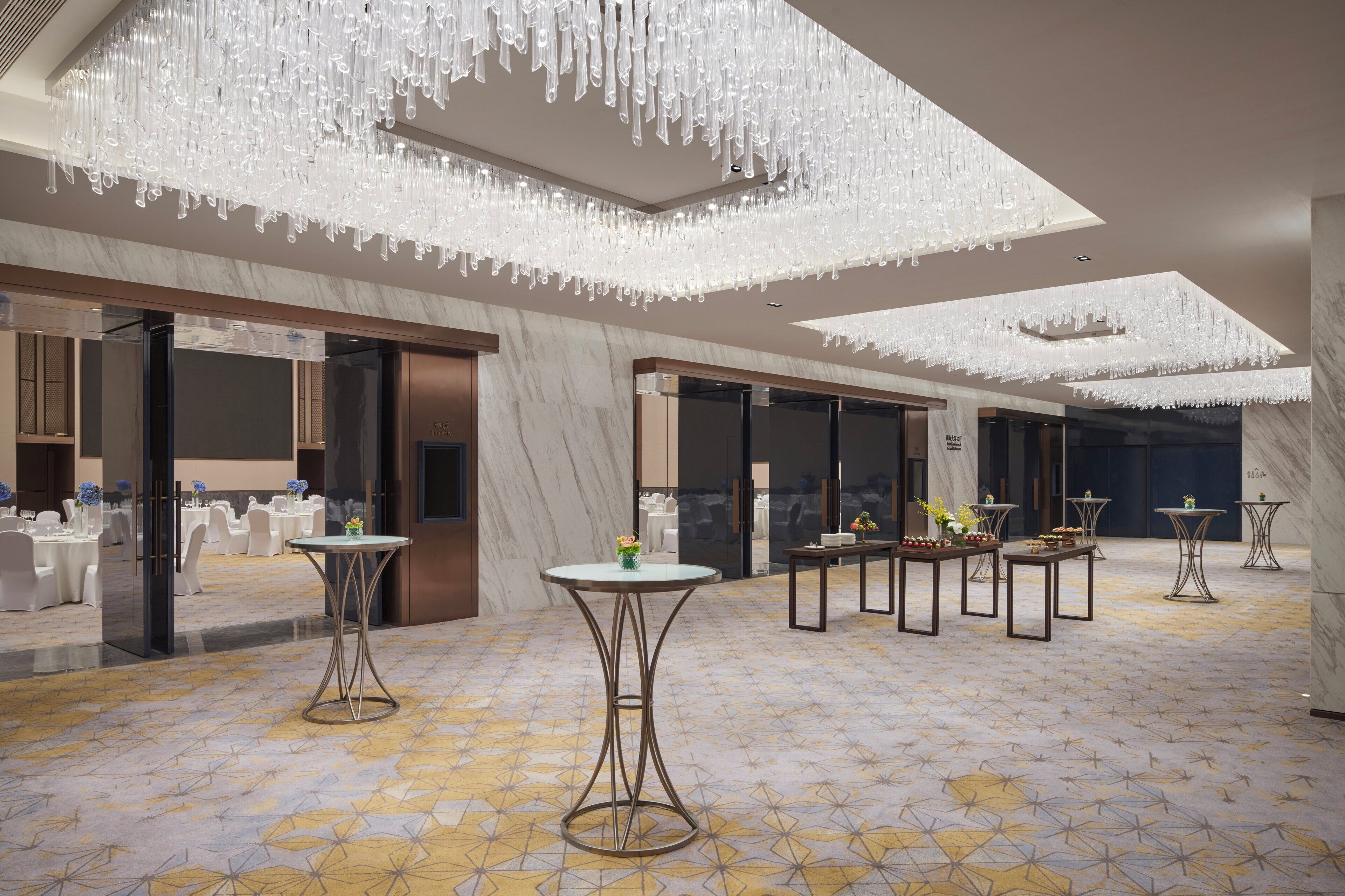 A hotel lobby with a marble floor, modern chandeliers, and round tables with floral centerpieces.