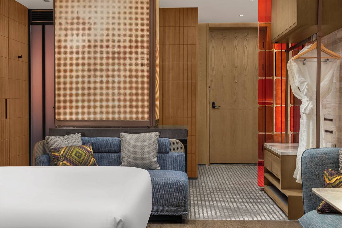 A modern hotel room with a large bed, a sofa, a desk, and a wardrobe.