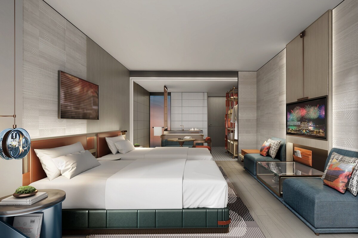Ett modernt hotellrum med en stor säng, en sittgrupp, en TV och utsikt över staden.
