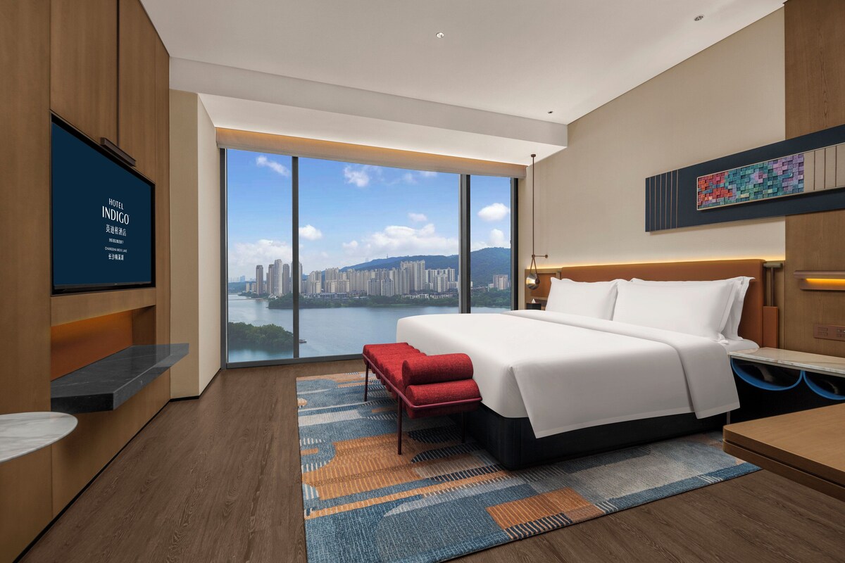A modern hotel room with a large bed, a TV, and a view of a cityscape.