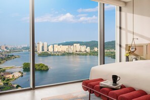 A bedroom with a large window offering a cityscape view, a bed with a red headboard, and a bedside table with a book and a mug. - Hotel Indigo Changsha Meixi Lake by IHG (Changsha)