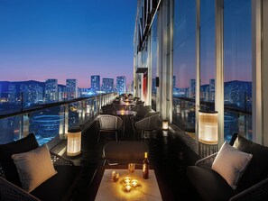 A rooftop bar with a city view, furnished with chairs and tables, and a bottle of wine on a table. - Hotel Indigo Changsha Meixi Lake by IHG (Changsha)