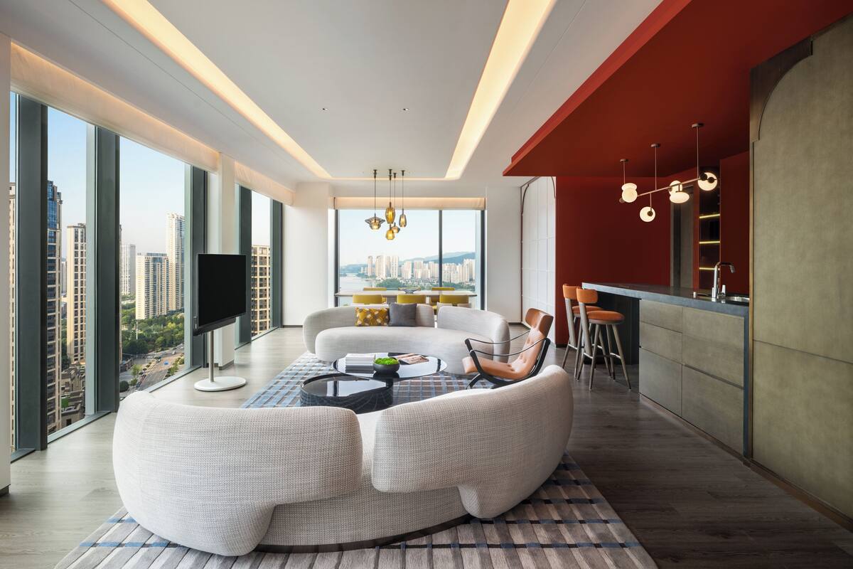 A modern living room with a sofa, a dining table, and a kitchen area with stools.