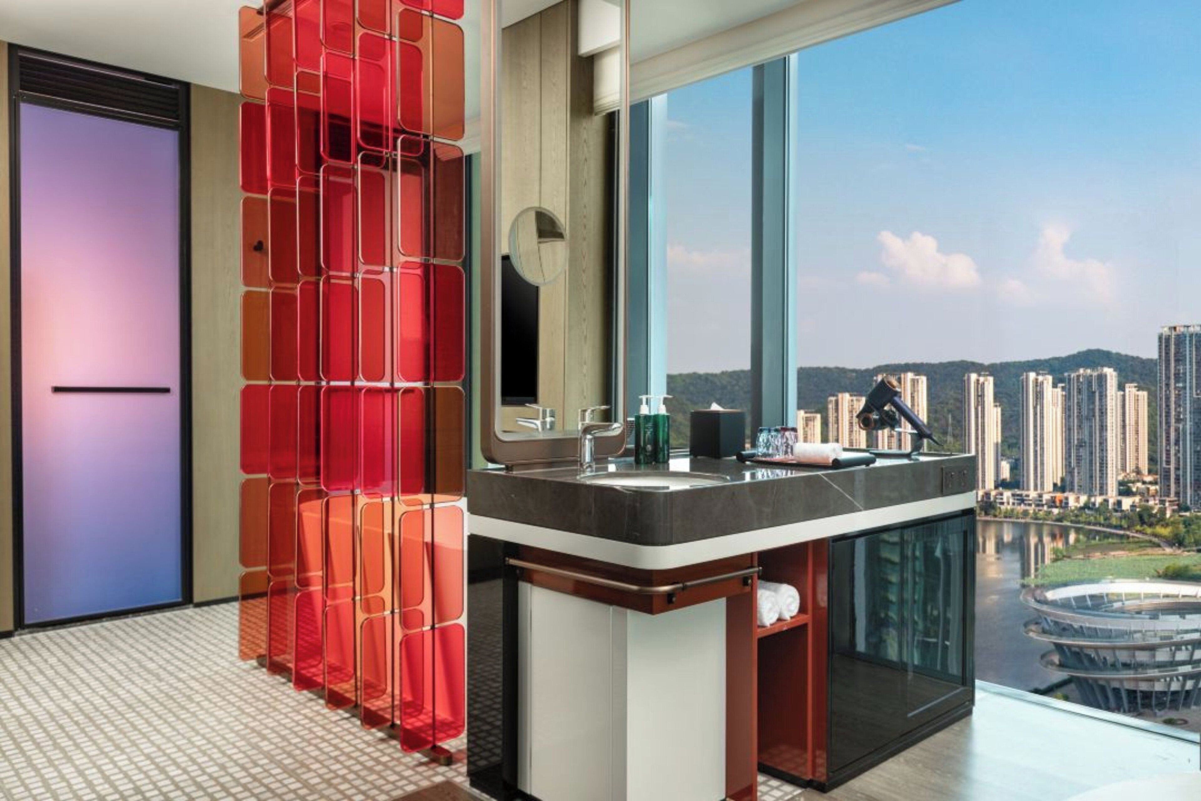 Un baño moderno con un ventanal amplio, cabina de ducha de vidrio y vistas a la ciudad.