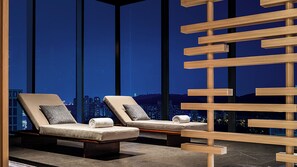 A modern lounge area with two cushioned chairs and a wooden slat structure, overlooking a cityscape at night. - Hotel Indigo Changsha Meixi Lake by IHG (Changsha)