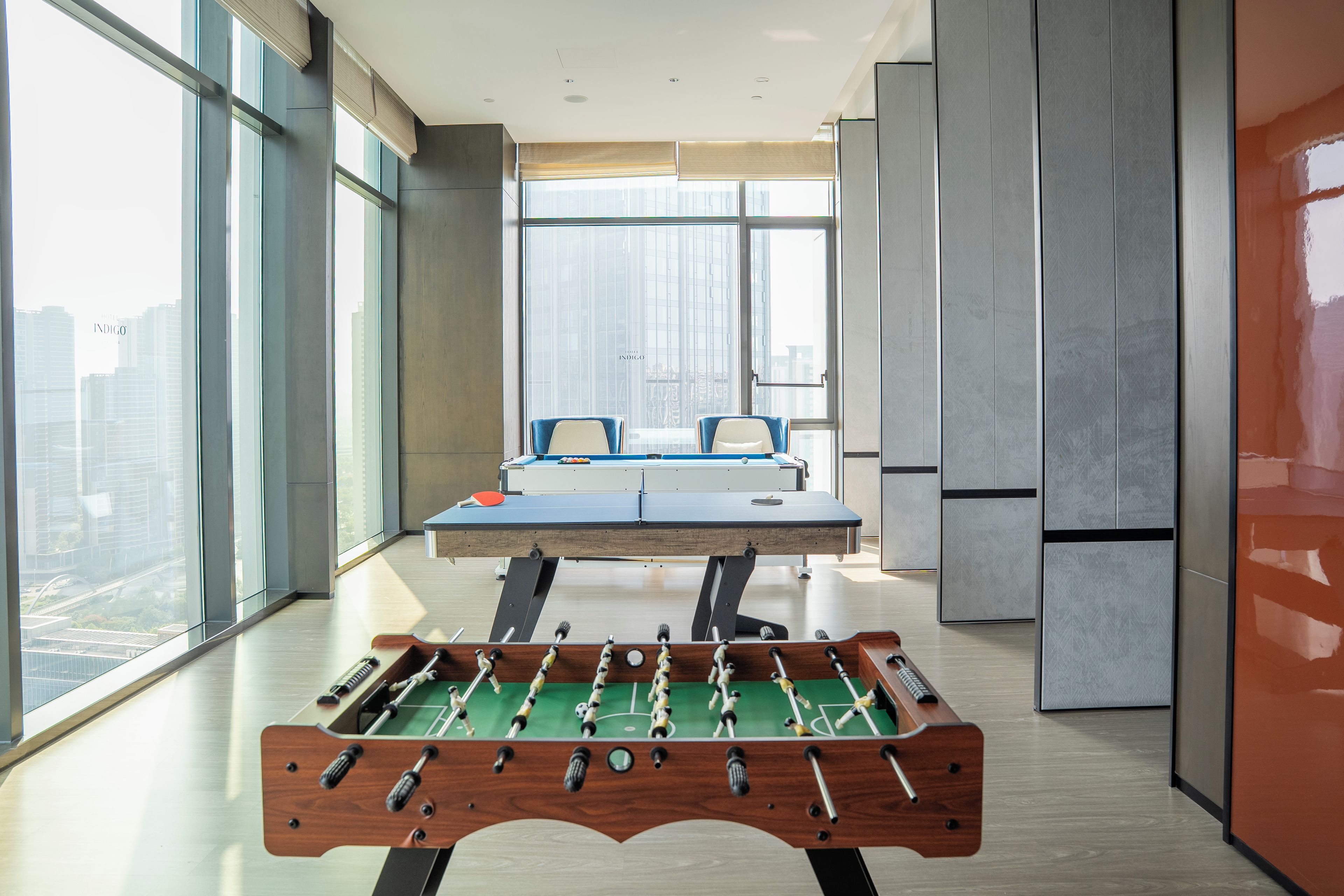 Una habitación moderna con mesa de fútbol de mesa, ventanas amplias y vistas a la ciudad.