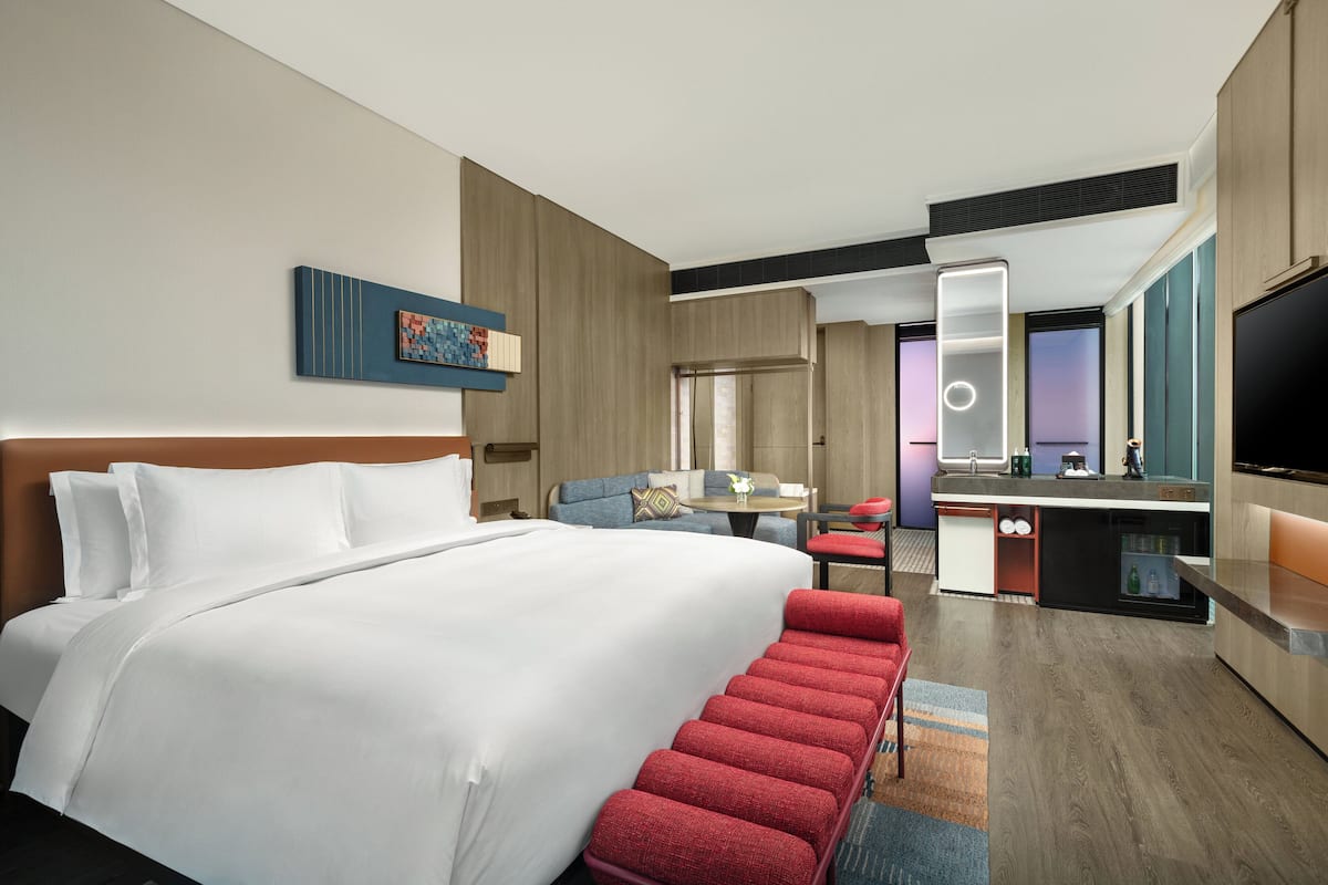 A hotel room with a large bed, a desk with a chair, a TV, and a bathroom with a mirror.