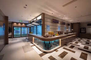 A modern hotel lobby with a curved reception desk, vending machines, and a tiled floor. - Holiday Inn Express Shanghai Pujiang Lianhang Road by IHG (Shanghai)