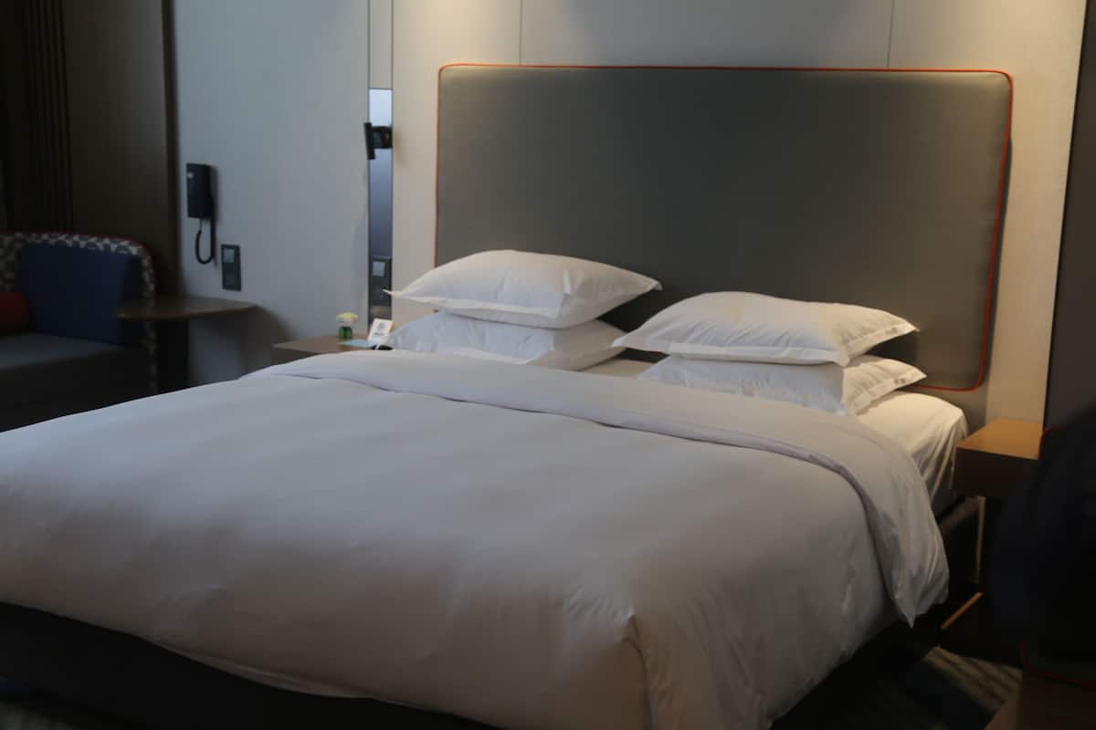 A neatly made bed with white linens and a headboard with a red trim.