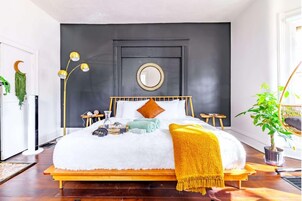 Un dormitorio moderno con cama, mesitas de noche, un espejo y una planta en maceta.