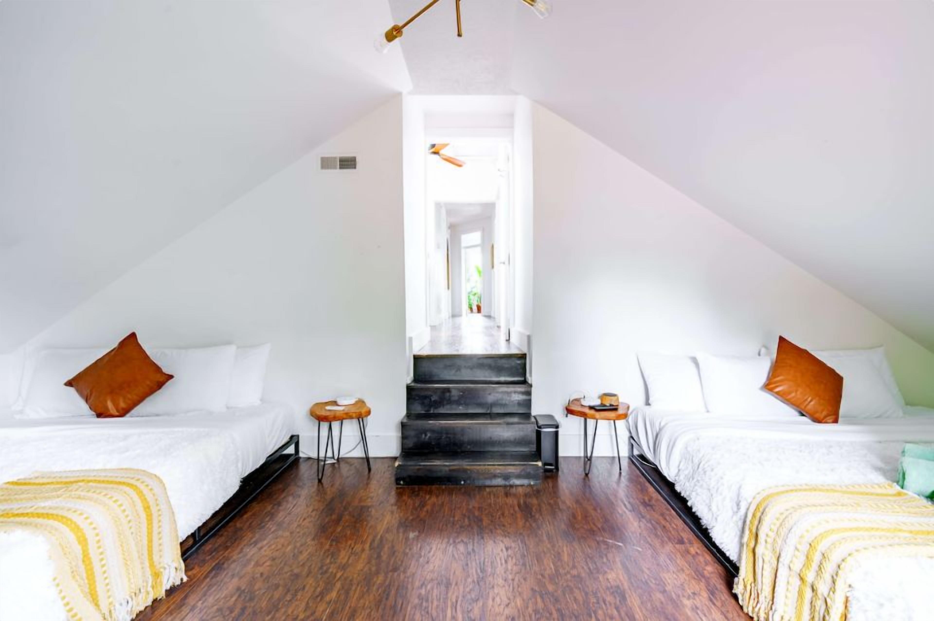 A room with two beds, a staircase, and a view through an open doorway.